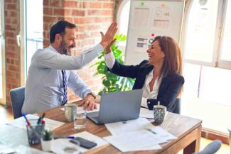 Two people at work high fiving at a desk